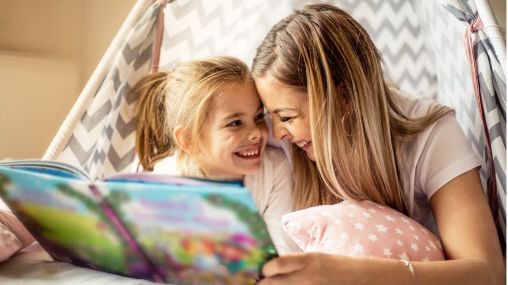 Mutter und Tochter lachen, während sie ihr vorliest Ursprung des Muttertags