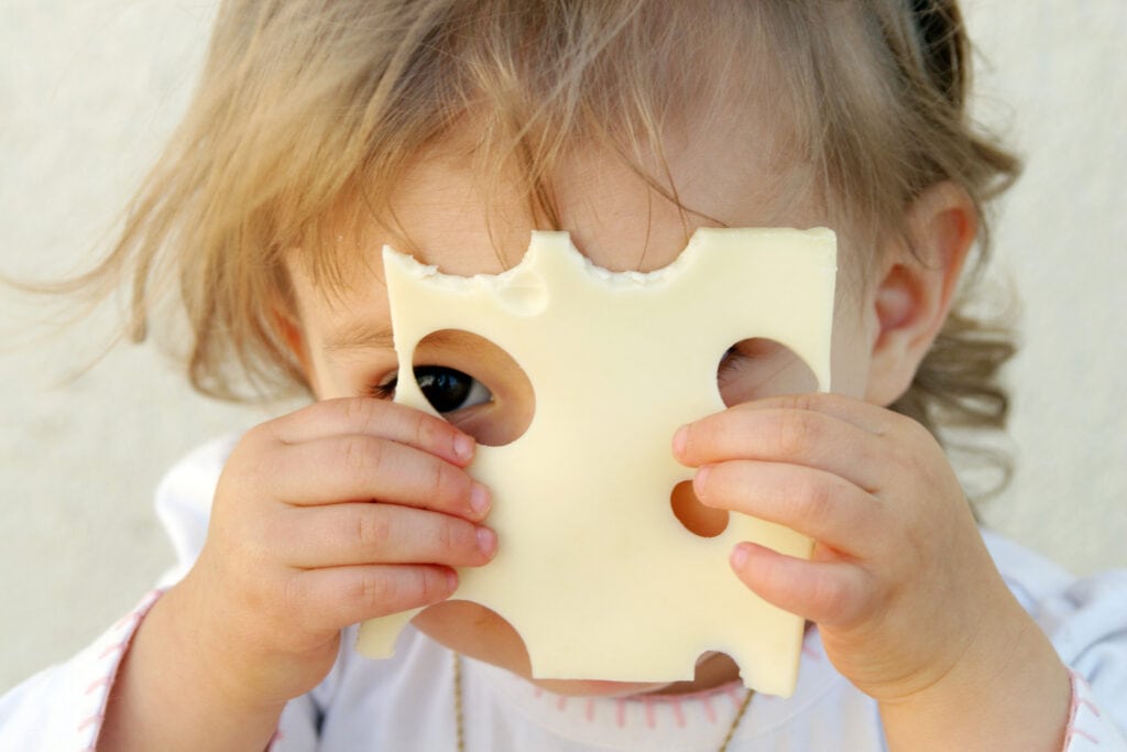 Kleines Kind mit Käse vorm Gesicht
