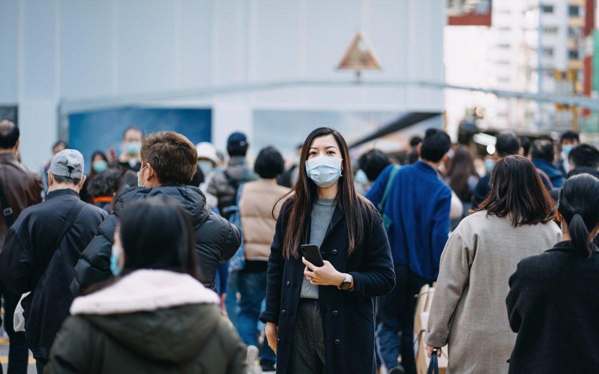 Frau mit Maske steht in Menschenmenge.