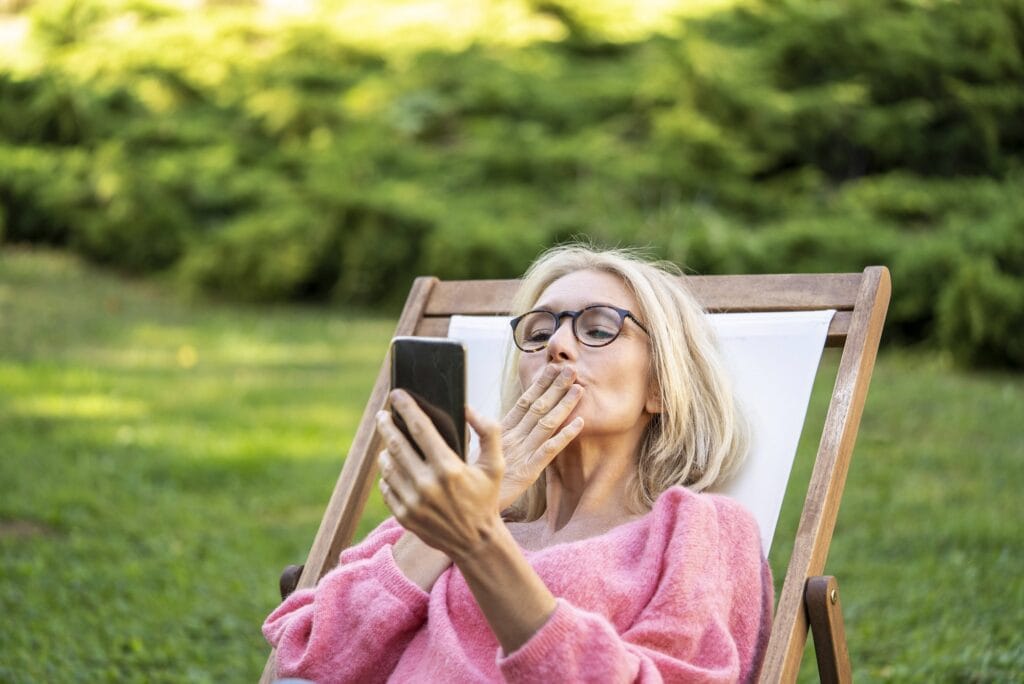 ältere Frau versendet einen Luftkuss per Smartphone