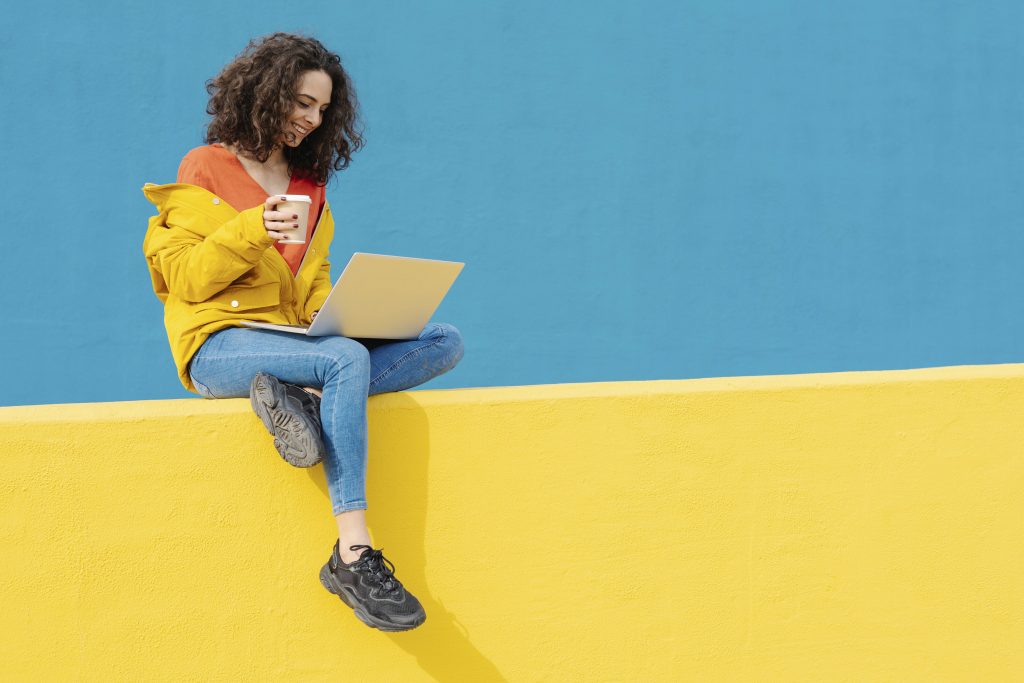 Frau mit Laptop und Kaffee vor buntem Hintergrund