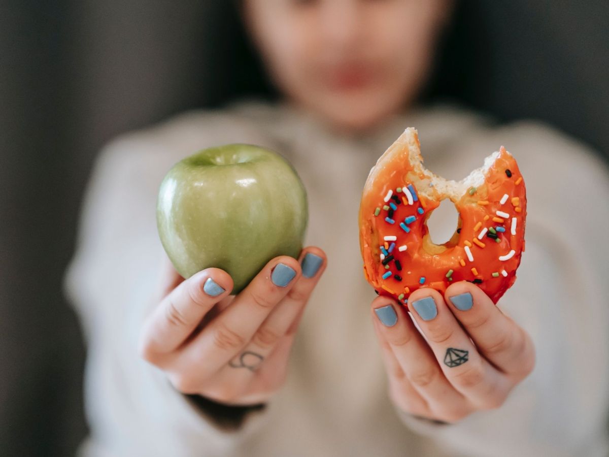 Frau hält Apfel und Donut hoch