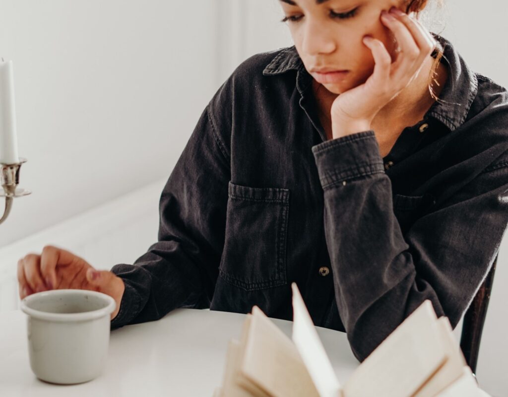 Frau sitzt mit Kaffeetasse vor Buch