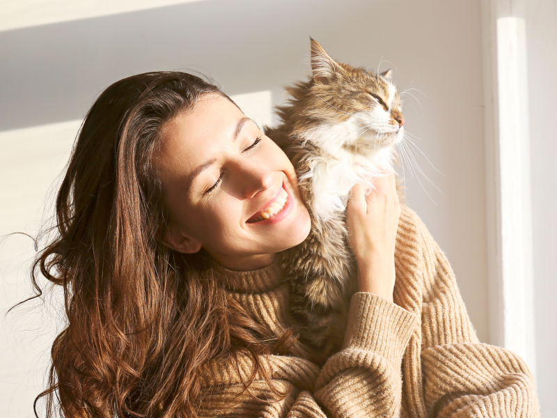 Frau hat Katze auf dem Arm und lacht.