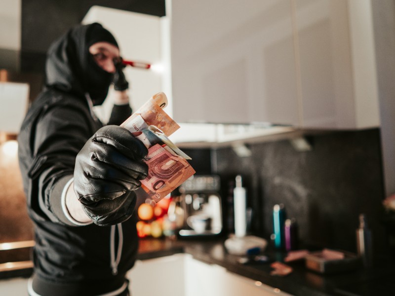 Ein Einbrecher hält Geldscheine in der Hand.