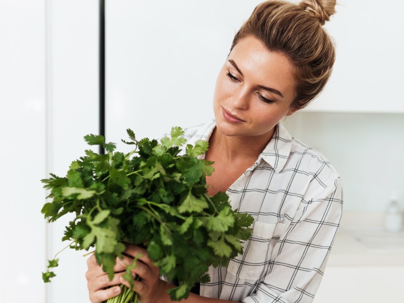 Frau mit Koriander Pflanze: Schmeckt er für dich auch nach Seife? Das ist der Grund