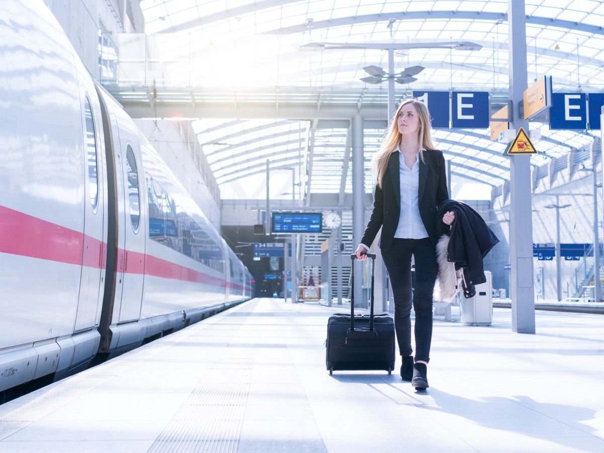 Eine Frau im Anzug geht mit ihrem Koffer an einem ICE entlang.