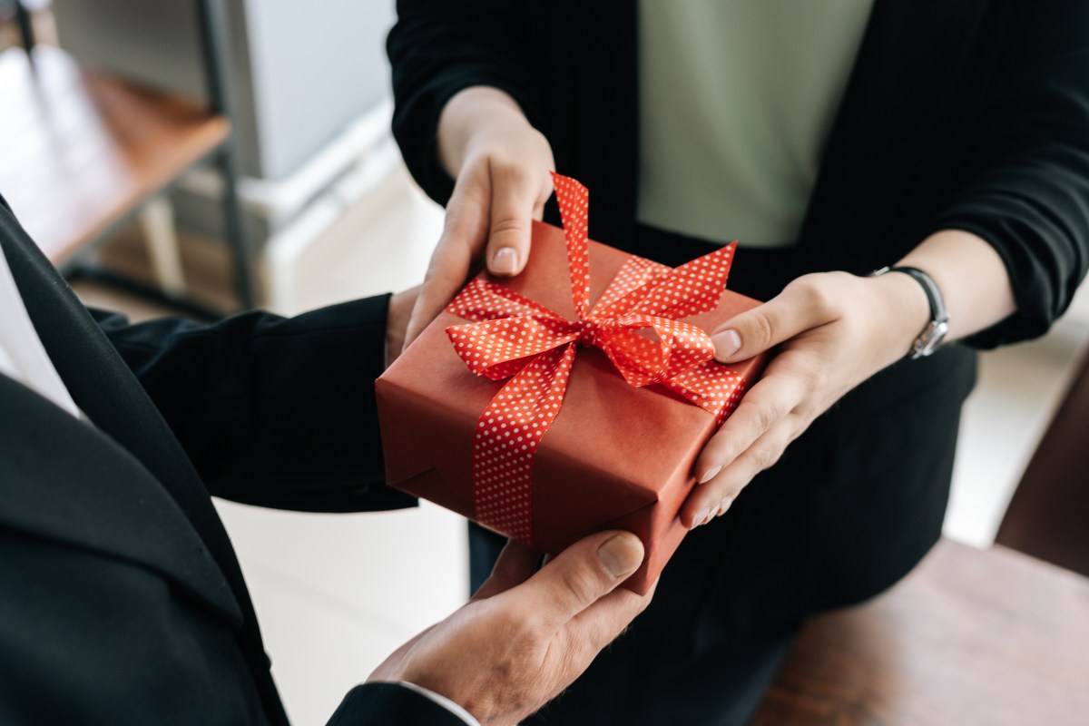 Eine Person übergibt ein Geschenk mit roter Schleife.