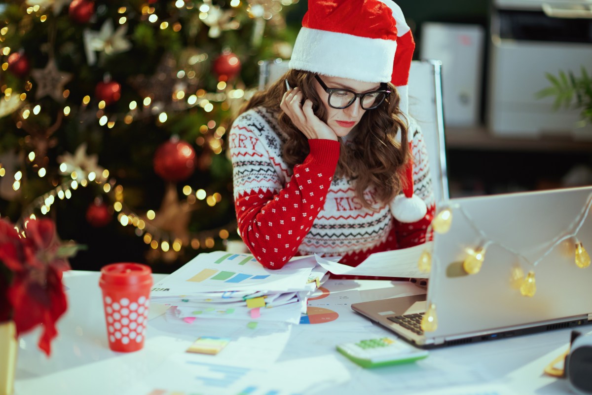 Frau sitzt vor Laptop. Die Stimmung ist weihnachtlich. Hinten steht ein Weihnachtsbaum.