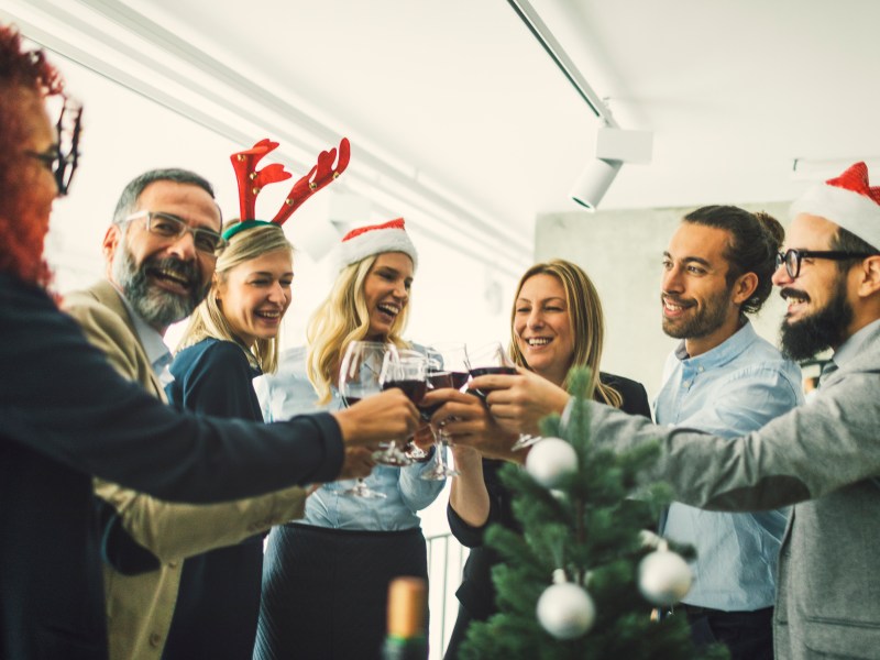 Eine Gruppe steht im Büro und stößt mit Wein an.