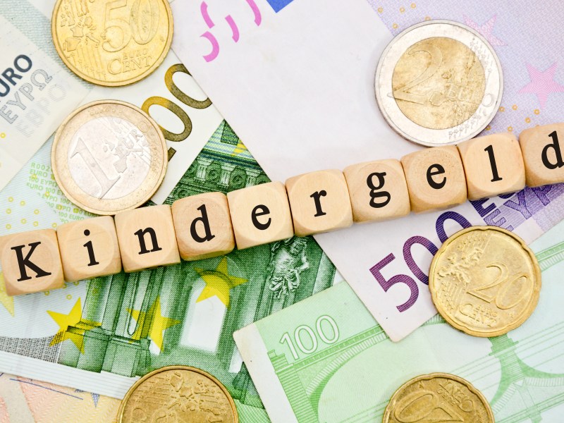 Auf Holzwürfeln steht das Wort "Kindergeld". Darunter liegen Geldscheine.