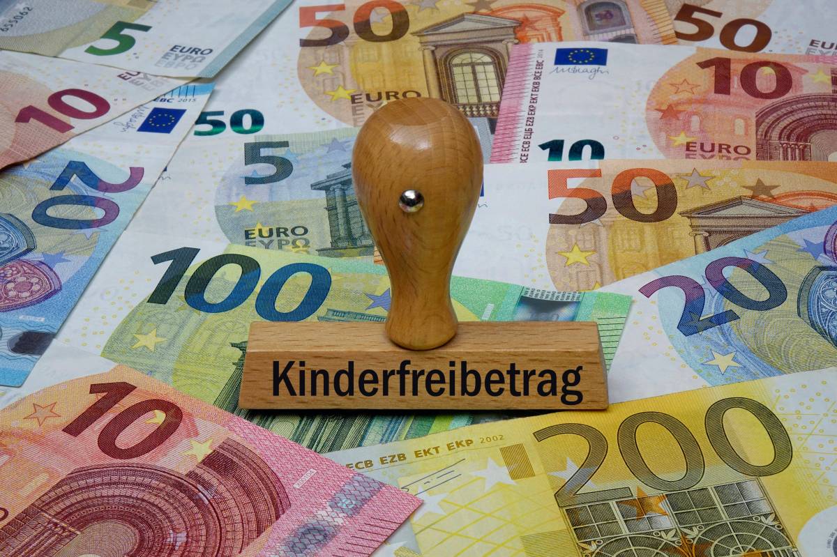 Auf einem Holzstempel steht das Wort "Kindergeld". Darunter liegen Geldscheine.