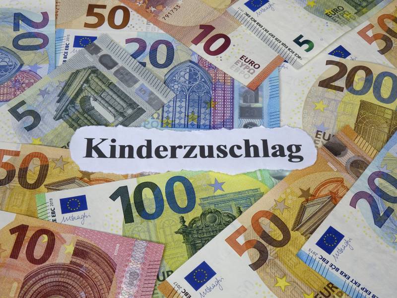 Auf einem weißen Zettel steht das Wort "Kinderzuschlag". Darum liegen Geldscheine.