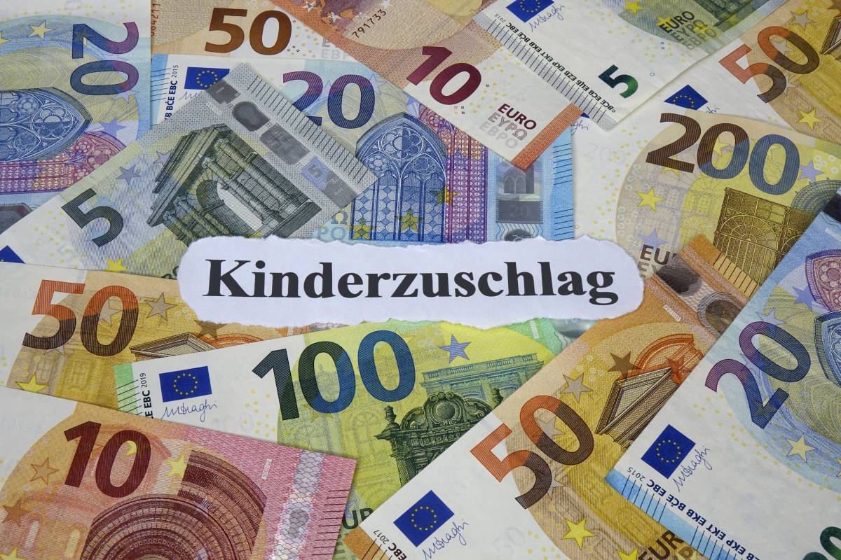 Auf einem weißen Zettel steht das Wort "Kinderzuschlag". Darum liegen Geldscheine.