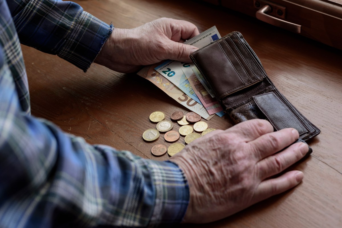 Ein Senior hat sein Portemonnaie geöffnet. Davor liegen Münzen und Geldscheine.