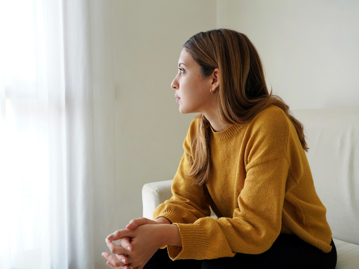 Eine junge Frau schaut traurig aus dem Fenster.