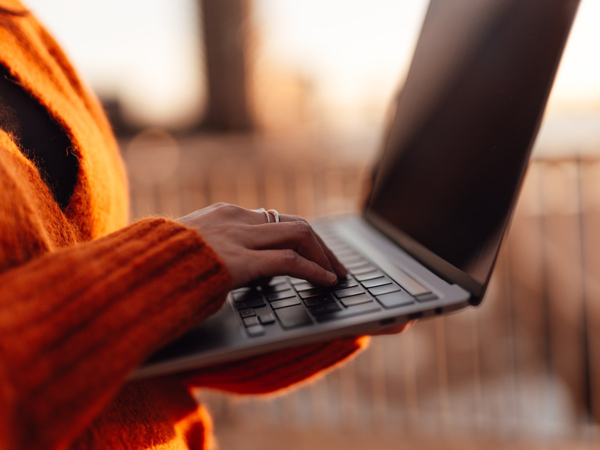 Frau tippt mit der Hand auf einer Laptop-Tastatur in einer Außenumgebung.