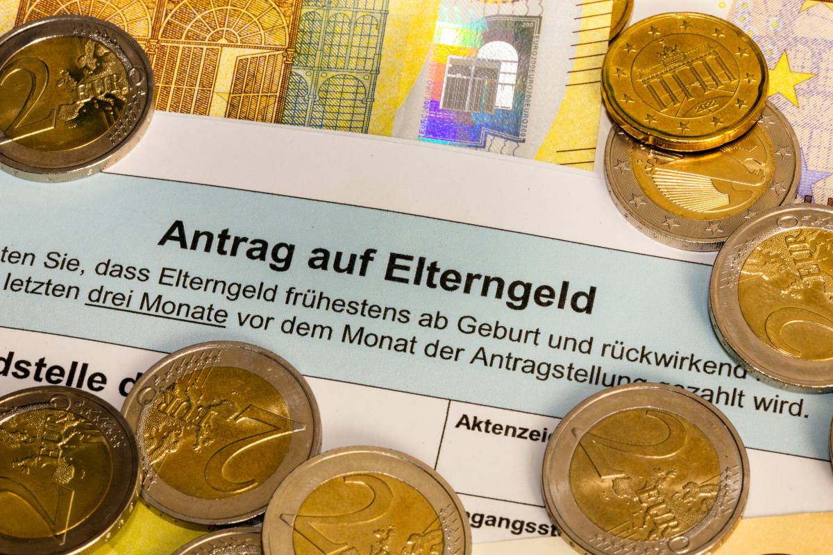 Zwischen Münzen und Geldscheinen liegt ein Antrag auf Elterngeld.