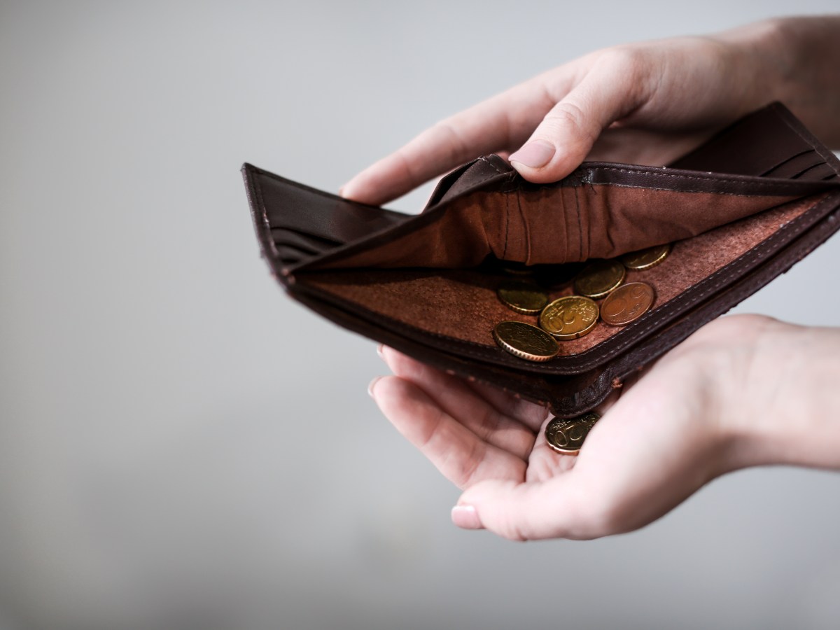 Eine Person hält ein Portemonnaie mit wenigen Münzen in der Hand.