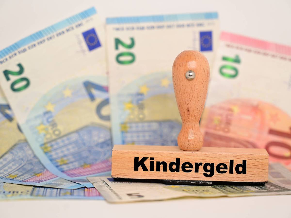 Auf einem Stempel steht das Wort "Kindergeld". Darunter liegen Geldscheine.