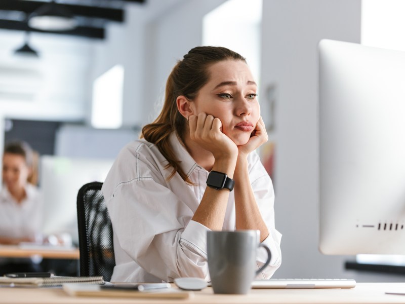 Eine Frau sitzt im Büro vor ihrem Computer und langweilig sich.