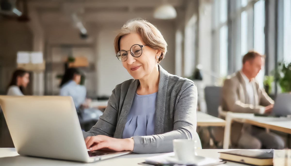 Eine ältere Dame sitzt im Büro am Computer.