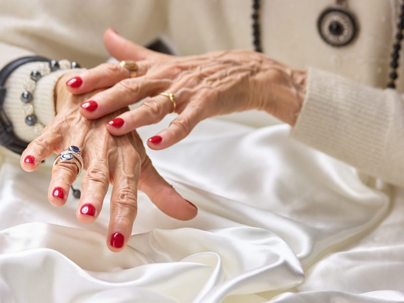 Hände einer alten Frau mit roten Fingernägeln