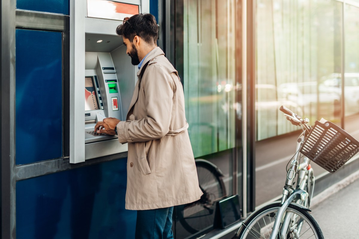 Ein Mann steht an einem Geldautomat und hebt Geld ab.