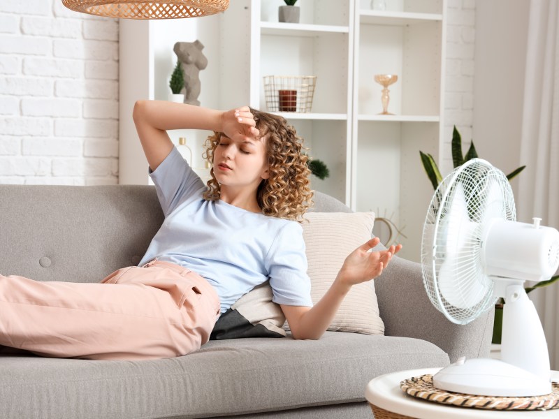 Eine Frau liegt auf dem Sofa. Ihr ist warm. Ein Ventilator ist auf sie gerichtet.