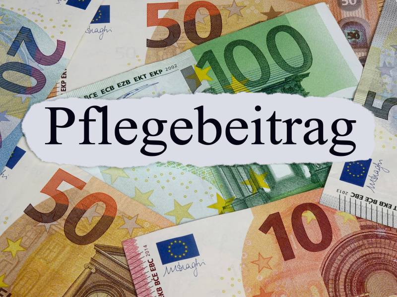 Auf einem weißen Zettel steht das Wort "Pflegebeitrag". Darunter liegen Geldscheine.