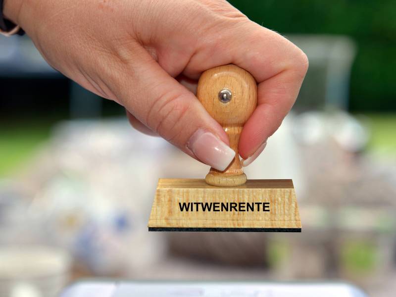 Eine Frau hält einen Stempel mit der Aufschrift "Witwenrente" in der Hand.