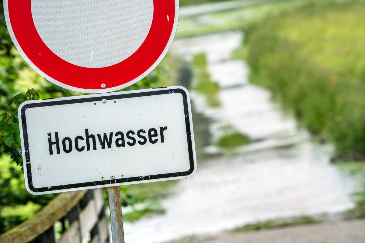 Auf einem Schild steht das Wort "Hochwasser". Dahinter ist ein gefluteter Weg.