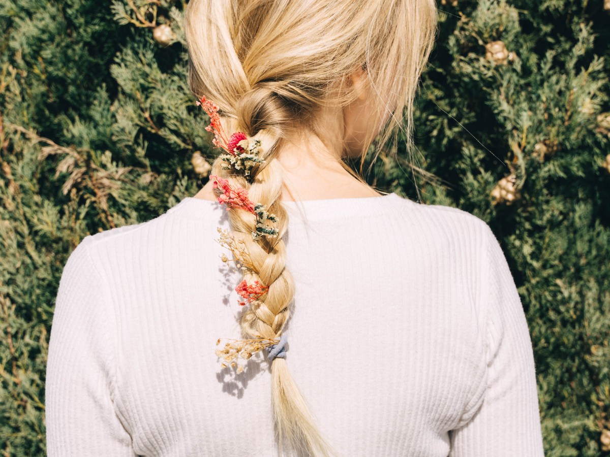 Blonde Frau mit Flechtfrisur und Blumen im Haar von hinten