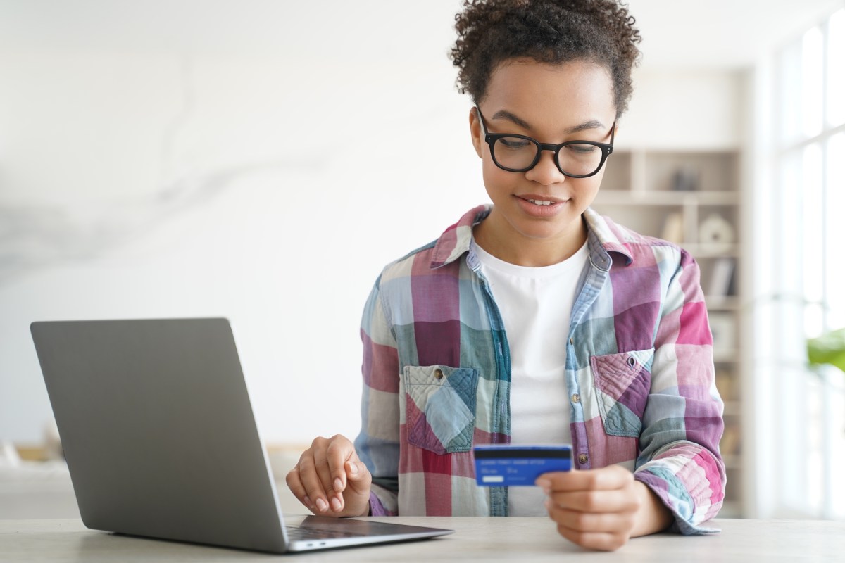 Eine Frau schaut auf ihre Bankkarte. Daneben ist ihr Laptop geöffnet.