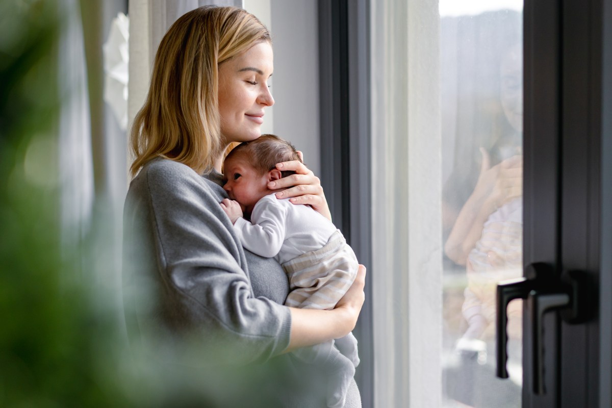 Eine Frau hält ein Baby auf dem Arm und schaut aus dem Fenster.