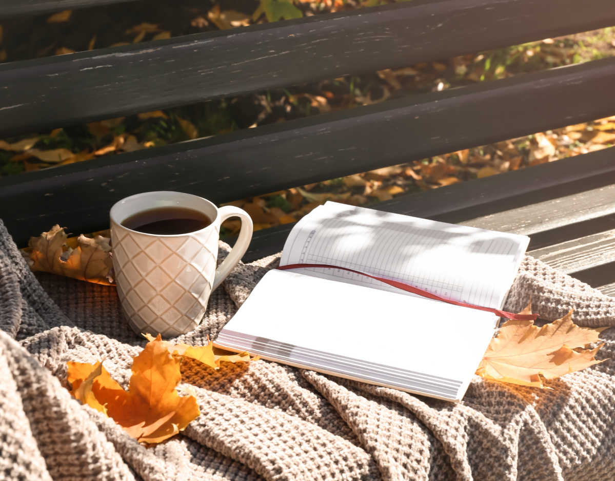 Decke, Tee und Buch im Herbst auf Parkbank