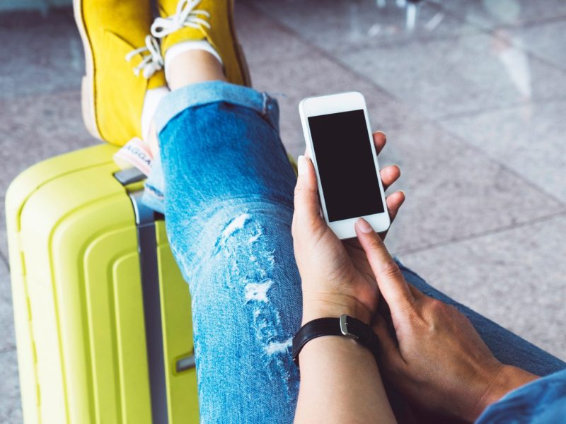 Frau mit Handy und Handgepäck am Flughafen