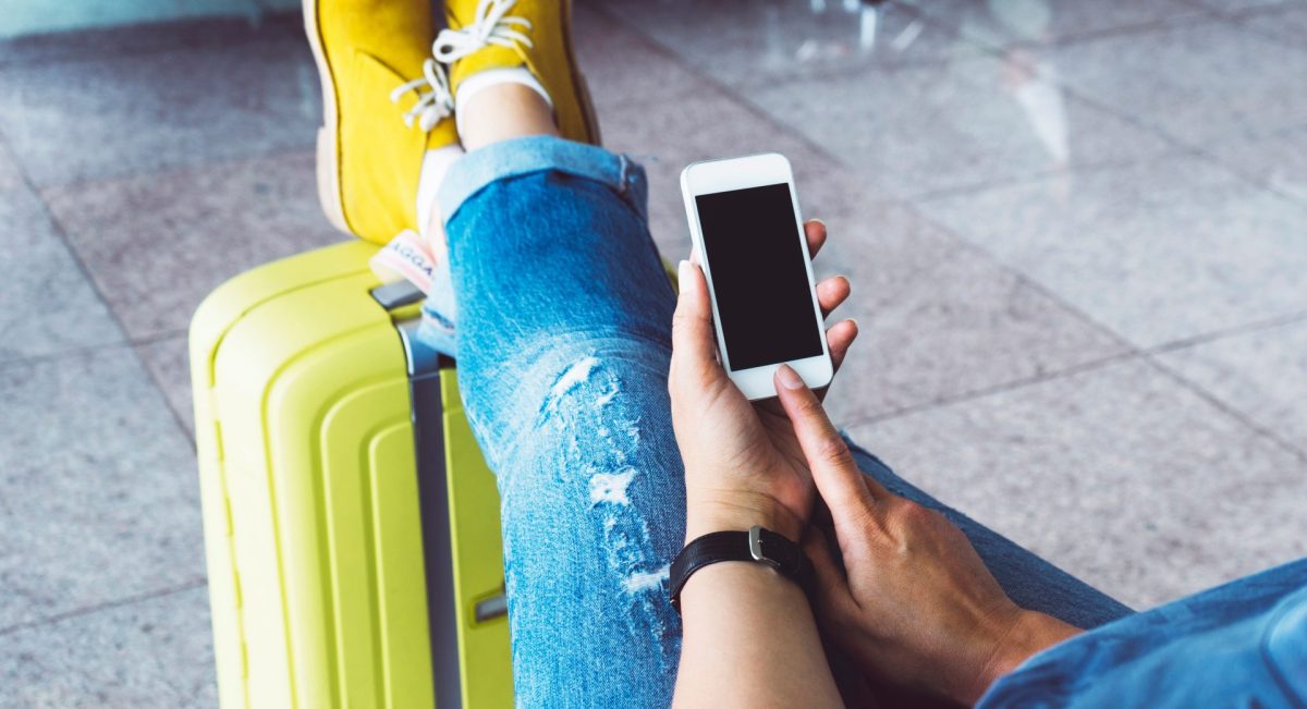 Frau mit Handy und Handgepäck am Flughafen