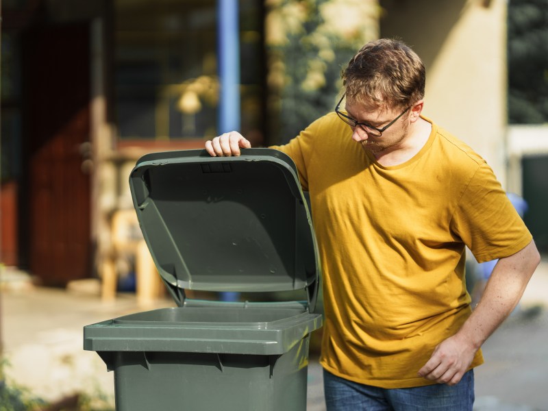 Eine Mann schaut in eine grüne Mülltonne.