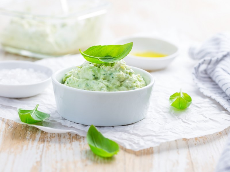 Avocado-Aufstrich mit Frischkäse in einer weißen Schale, garniert mit Basilikum.