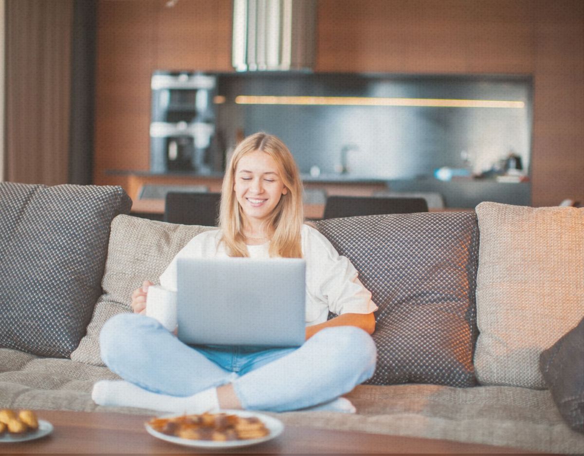 Eine junge Frau sitzt auf dem Sofa und schaut auf ihren Laptop.