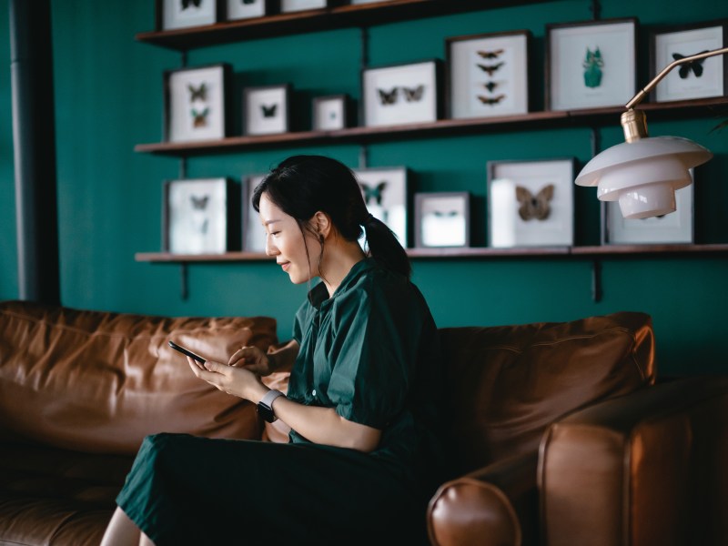 Eine Frau sitzt auf dem Sofa und schaut in ihr Online-Banking.