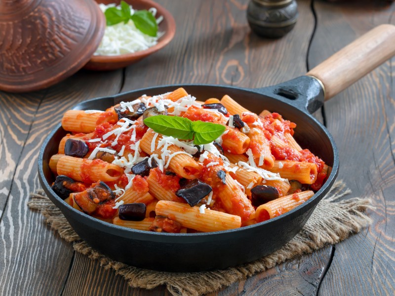 Pasta alla Norma in einer gusseisernen Pfanne mit Pecorino und Basilikum.