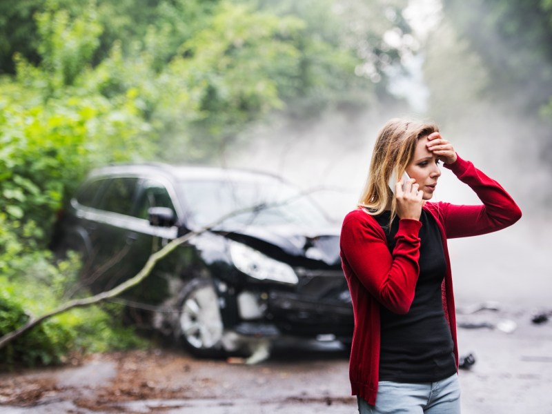 Frau steht vor einem kaputten Auto nach Unfall