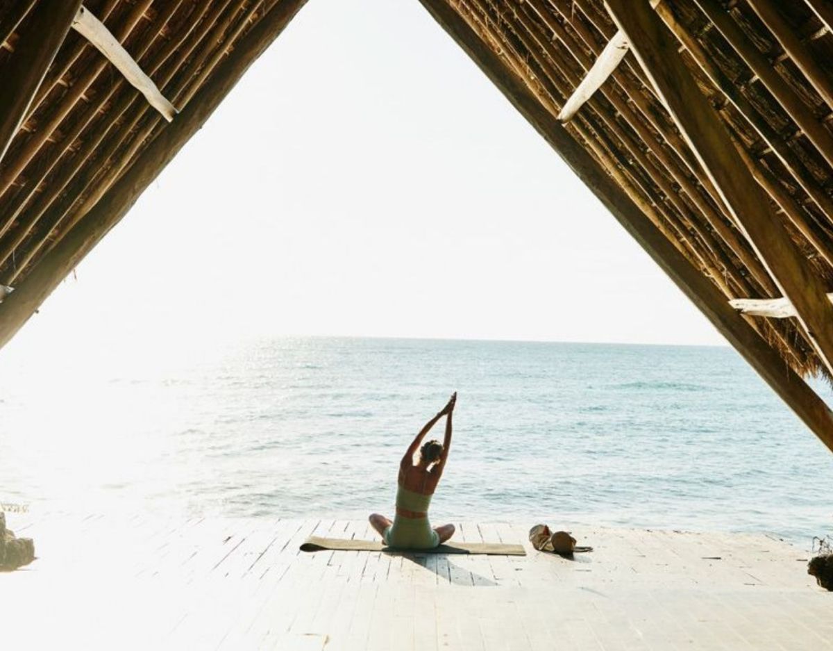 Frau sitzt am Strand und macht Yoga