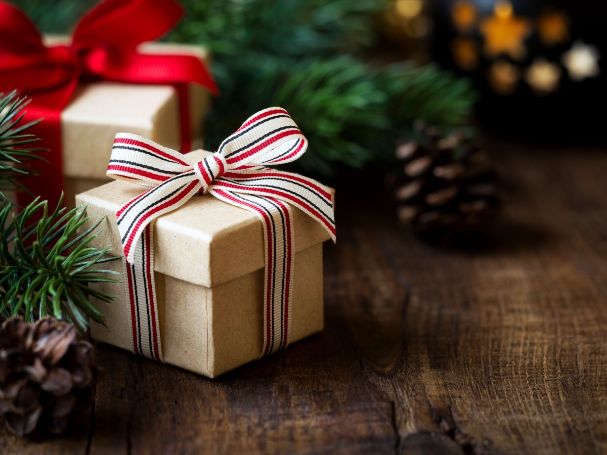 Weihnachtsgeschenk auf einem dunklen rustikalen Holztisch mit Tannenzapfen und Tannenzweigen.