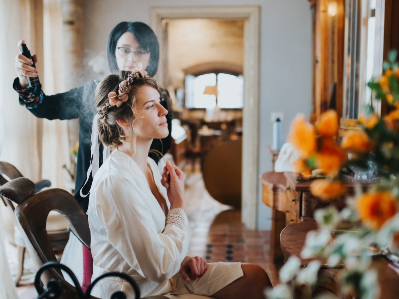 Eine junge Frau macht einer Frau die Haare. Sie versprüht Haarspray. Ausbildung Jobs