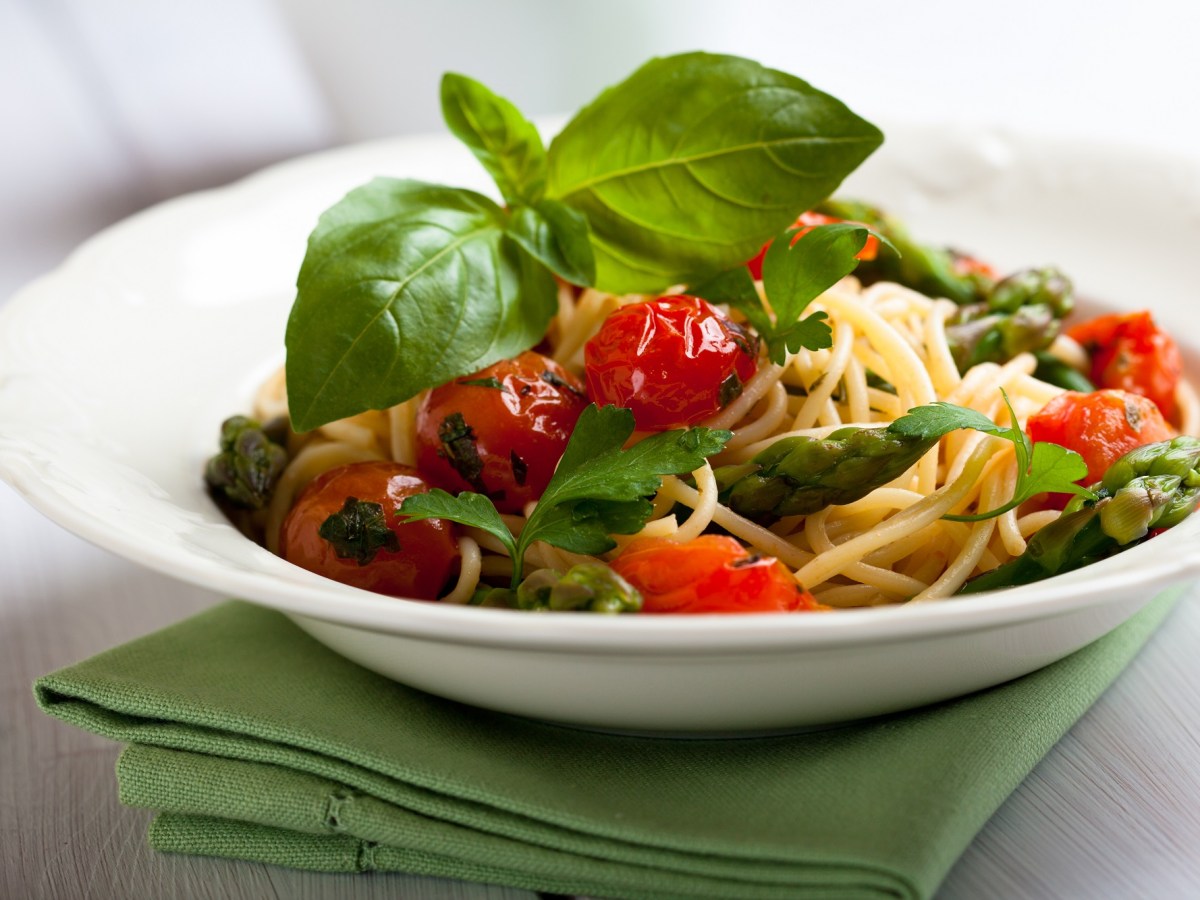 Teller mit Spaghetti mit geschmolzenen Tomaten und grünem Spargel.