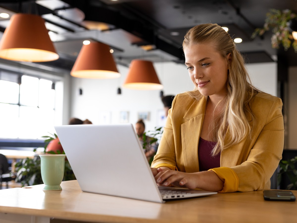 Eine Frau mit blonden Haaren sitzt im Büro und arbeitet am Laptop.