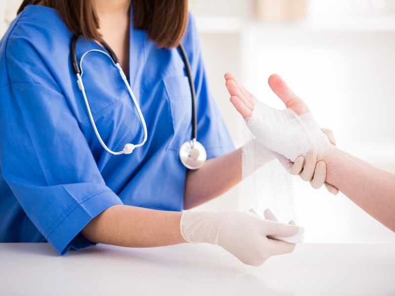 Nahaufnahme einer Ärztin bandagiert die Hand eines Patienten beziehungsweise einer Patientin.